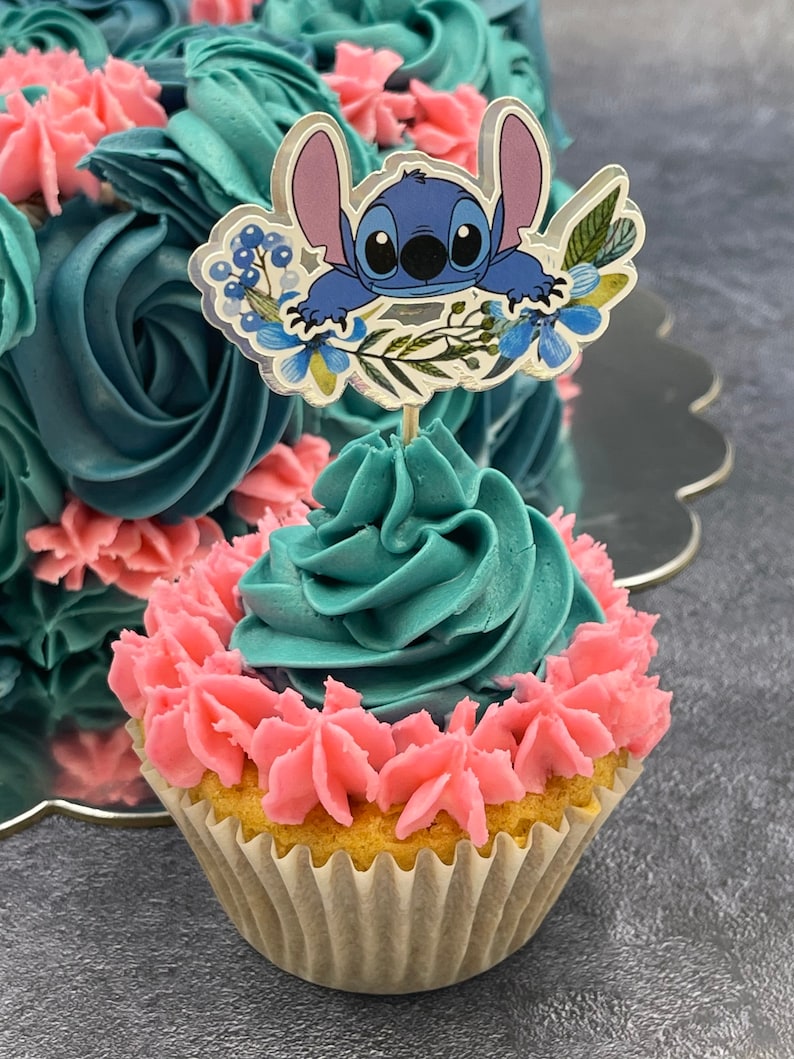 K&ouml;nnte beinhalten: Ein t&uuml;rkisfarbener und rosafarbener Cupcake mit einem blauen Comic-Charakter als Topper. Der Charakter ist Stitch aus dem Disney-Film Lilo & Stitch. Der Cupcake ist mit rosa und t&uuml;rkisfarbenem Frosting verziert.