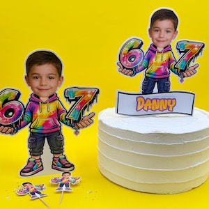 May include: A birthday cake with a white frosting and a cake topper. The topper features a cartoon image of a boy holding the numbers 6 and 7. The name "Danny" is written on the topper. The background is yellow.