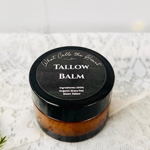 Könnte beinhalten: Ein kleiner Braunglastiegel mit Talgbalsam und einem schwarzen runden Etikett. Das Etikett trägt den Text What Calls the Heart, TALLOW BALM und Ingredients: 100% Organic Grass Fed Bison Tallow in weißer und grauer Schrift aufgedruckt.