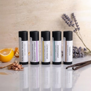 May include: Five cylindrical lip balm tubes with black caps and white labels. The labels are printed with the text: Pure Bison Tallow, Vanilla Lavender, Citrus Fresh, Peppermint, and Vanilla. Each tube features a unique colored accent stripe.