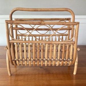 Puede incluir: Un revistero de bambú tejido natural con un patrón de cruz decorativo. El revistero tiene una forma rectangular y está hecho de bambú marrón claro.