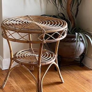 May include: A round, two-tiered, woven rattan side table with a natural brown finish. The table has a circular top and bottom shelf with a spiral design.