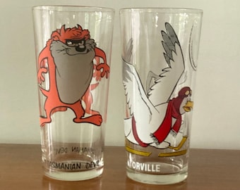May include: Two vintage cartoon character glasses. The glass on the left features Taz the Tasmanian Devil in orange and grey. The glass on the right features a white bird with a red scarf and the text "Orville".