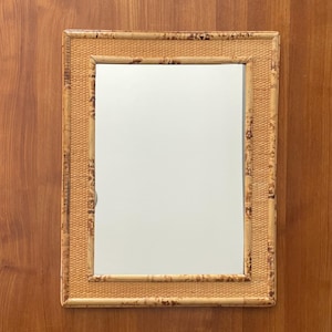 以下が含まれることがあります： 編み込まれた竹フレームの長方形の鏡。 フレームは自然な薄茶色で、濃い茶色のアクセントがあります。 鏡は木製の表面に取り付けられています。