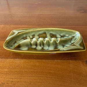 May include: A green and white ceramic ashtray with a wavy design. The ashtray has five indentations for cigarettes.