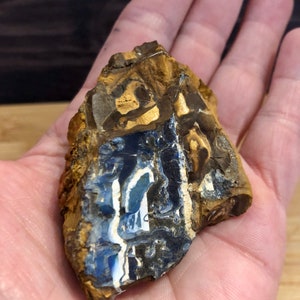 Peut inclure: Un morceau d'opale bleu et blanc de forme irrégulière et rugueuse avec une matrice brune et noire. L'opale présente un motif tourbillonnant de bleu, de blanc et de noir.
