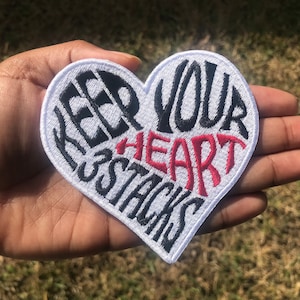 May include: White heart-shaped patch with black embroidery that reads "Keep Your Heart Stacks" in a stylized font. The word "heart" is embroidered in red.