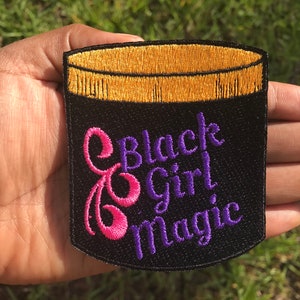 May include: Black embroidered patch with a gold rimmed jar and the text "Black Girl Magic" in purple and pink lettering.