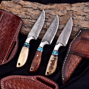 May include: Three Damascus steel knives with turquoise accents and wooden or bone handles. The blades have a unique pattern. Brown leather sheaths with decorative stitching are also visible, set against a dark background.