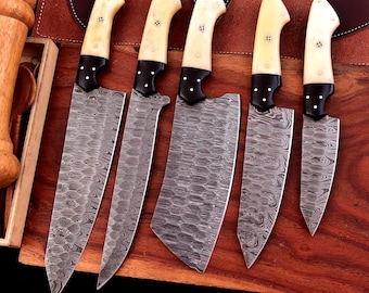May include: Set of five kitchen knives with bone handles and Damascus steel blades. The knives are arranged on a wooden surface.