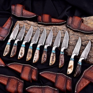 May include: An assortment of handcrafted knives with patterned blades and turquoise accents. The handles are made of bone and wood. Each knife is paired with a brown leather sheath. The blades are approximately 8 inches long.