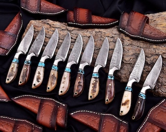 May include: An assortment of handcrafted knives with patterned blades and turquoise accents. The handles are made of bone and wood. Each knife is paired with a brown leather sheath. The blades are approximately 8 inches long.