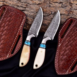 May include: Two Damascus steel knives with bone handles and turquoise accents. The blades have a unique pattern, and the handles are cream-colored. Each knife has a leather sheath with a basket weave design. The sheaths are brown and have white stitching.