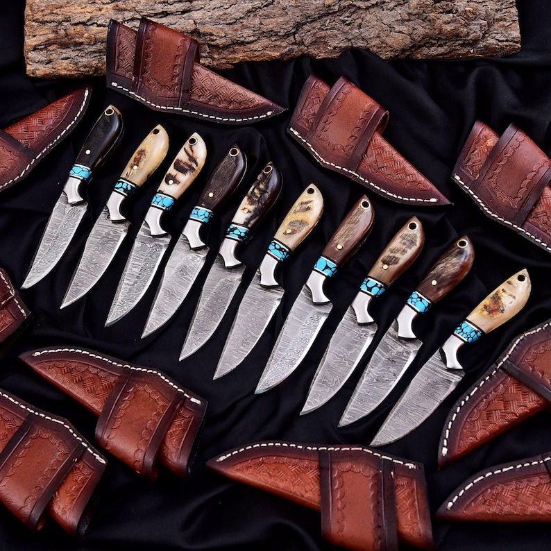 May include: An array of handcrafted knives with patterned blades and various handle designs, including wood and bone, accented with turquoise. Each knife is paired with a brown leather sheath. The knives are arranged on a black surface.