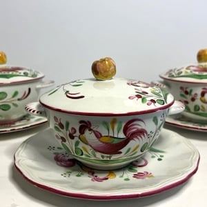 May include: Three ceramic soup bowls with lids and saucers. The bowls are white with a red rim and feature a rooster design. The lids have a yellow knob and floral patterns. The saucers have a matching design.