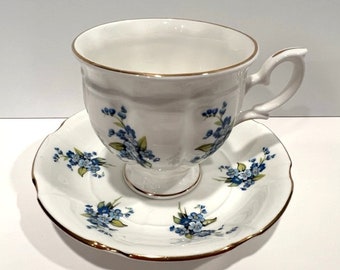 May include: White teacup and saucer set with a floral design. The teacup has a gold rim and a handle. The saucer has a scalloped edge and a matching floral pattern. The teacup and saucer are made of porcelain.
