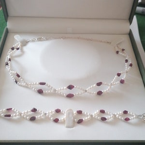 May include: A two-strand pearl necklace and bracelet set with red gemstone accents. The necklace and bracelet are both made of white pearls and red gemstones.