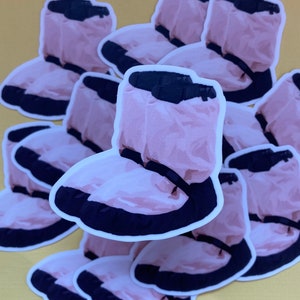 May include: A stack of pink and black waterproof shoe covers. The shoe covers are made of a crinkled material and have a black elastic band around the top.