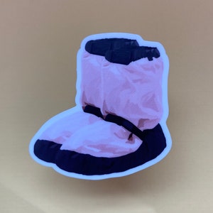 May include: A pink and black fuzzy boot sticker. The boot is puffy and has a black strap across the top.