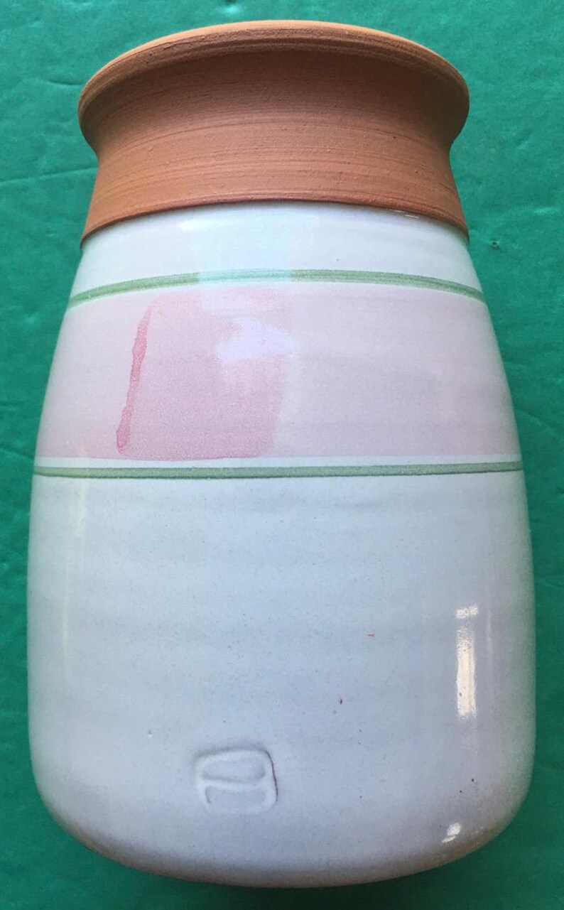 May include: A handmade ceramic vase with a light blue base, a pink band, and a terracotta rim. The vase features green stripes and a unique, rounded shape. The bottom has a stamped design.
