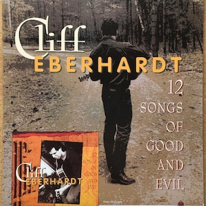 May include: A poster advertising a music album by Cliff Eberhardt. The poster features a photo of Eberhardt playing a guitar in a forest setting. The album title is "12 Songs of Good and Evil" and the album is available on Red House Records.