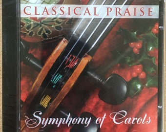 May include: A CD case with a red, green, and gold background. The case features a close-up of a violin with the text "Classical Praise Symphony of Carols" printed on the front.