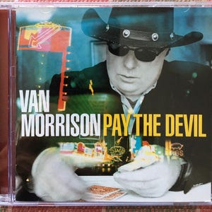 May include: A CD cover featuring a black and white photo of Van Morrison, wearing a cowboy hat and sunglasses, with the title "Pay the Devil" in yellow text.
