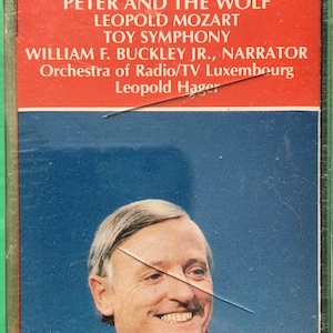 May include: A cassette tape with a red and white label featuring the title "Prokofiev Peter and the Wolf" and the names "Leopold Mozart, Toy Symphony, William F. Buckley Jr., Narrator, Orchestra of Radio/TV Luxembourg, Leopold Hager". A smiling man is pictured on the front of the cassette tape.