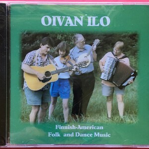 May include: A CD cover featuring a group of four people playing musical instruments outdoors. The cover is green with the title "Oivan Ilo" in white text and the words "Finnish-American Folk and Dance Music" in black text.