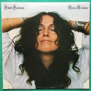 May include: A vinyl record album cover featuring a woman with long, dark hair. The album title is "Sweet Harmony" and the artist is "Maria Muldaur".