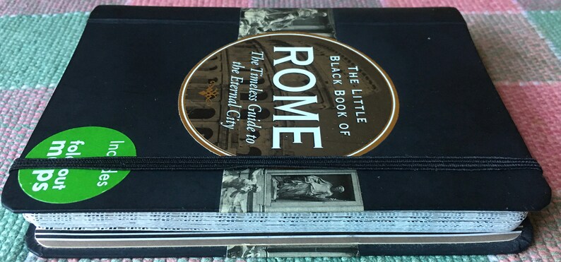 Pu&ograve; includere: Un libro nero con un adesivo dorato che dice "The Little Black Book of Rome" e "The Timeless Guide to the Eternal City". Il libro ha un elastico nero e un adesivo verde che dice "Includes fold out maps".