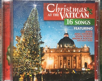 May include: A CD case with a Christmas theme featuring a large Christmas tree and St. Peter's Basilica in the background. The text on the case reads "Christmas at the Vatican 16 Songs Featuring Jewel, Josh Groban, John Denver, Andrea Bocelli and many more."