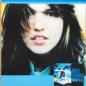 May include: A promotional poster for Bree Sharp. The poster features a close-up of a woman's face with the name "BREE SHARP" in large blue letters at the top. A smaller image shows the artist leaning against a taxi.