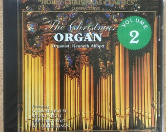 May include: A compact disc case with a picture of a pipe organ on the front. The title of the album is "The Christmas Organ" and the album is volume 2 of the "Holly Christmas Classics" series. The album features the music of organist Kenneth Abbott.