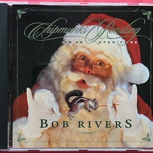 May include: A red and white Santa Claus figure holds a small brown and white chipmunk on a stick. The text "Chipmunks Roasting on an Open Fire" is above the figure and "Bob Rivers" is below the figure. The background is black with a green holly border.