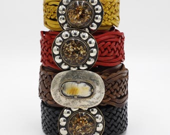 May include: Four stacked leather bracelets in yellow, red, brown, and black. Each bracelet has a woven design. The top three bracelets have round, silver-toned buckles with a textured center. The third bracelet has an oval buckle.