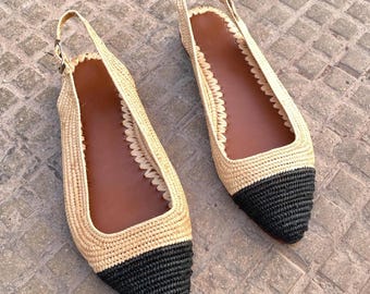 May include: A pair of beige and black woven slingback flats. The shoes have a pointed toe with a black woven design, a beige woven upper, and a brown insole. The slingback strap is secured with a small gold buckle.