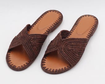 May include: A pair of brown woven sandals with a light brown footbed. The sandals have a crisscross design on the top and a stitched border. The footwear is displayed on a white background.