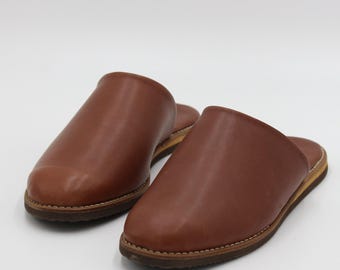May include: A pair of brown leather slippers with a closed toe and an open back. The slippers have a simple design and a comfortable look.