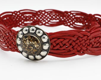 May include: A red leather belt with a woven design. The belt features a silver-toned buckle with a decorative center. The belt is approximately 1.5 inches wide and is suitable for waist sizes up to 36 inches.