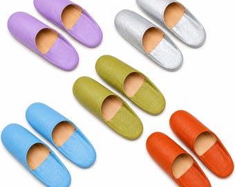 May include: Five pairs of slip-on slippers in various solid colors including lavender, silver, olive green, light blue, and orange. Each pair features a rounded toe, an open heel, and a tan interior lining, arranged in a scattered pattern.