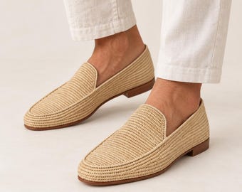 May include: A pair of beige woven loafers featuring a textured straw-like material, a rounded toe, and a low brown heel. The slip-on shoes have a structured silhouette with a clean finish, paired with white trousers that end above the ankle.