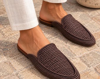 May include: A pair of dark brown woven mules featuring a textured, braided upper design with a rounded toe and a flat, smooth sole. These slip-on shoes have an open back and a structured silhouette, providing a clean look for casual footwear.