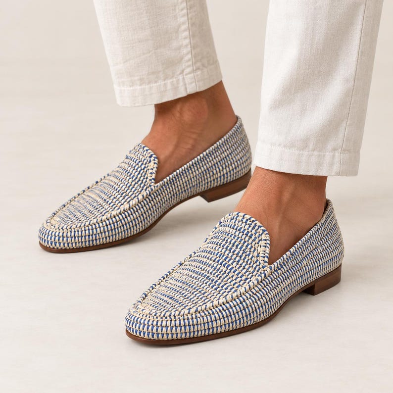 May include: A pair of slip-on loafers featuring a woven texture in alternating blue and cream threads. The shoes have a low-profile silhouette with a rounded toe, a visible stitched seam along the top, and a flat brown sole with a small heel.