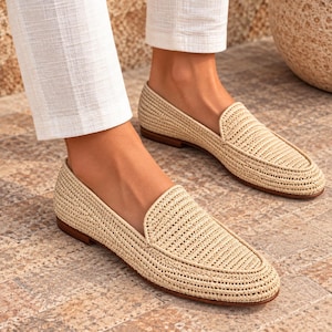May include: A pair of beige woven loafers featuring a textured straw-like material, a rounded toe, and a low brown heel. The slip-on shoes have a structured silhouette with a reinforced trim around the opening and a flat, durable sole construction.