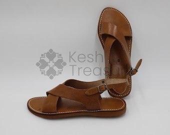 May include: Two pairs of brown leather sandals with criss-cross straps and buckles. The sandals have a simple design and are made of high-quality leather.