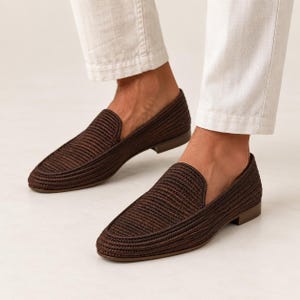 May include: A pair of dark brown woven loafers with a textured, braided surface and a low heel. The shoes feature a slip-on design with a rounded toe and a solid, matching brown sole, providing a clean and uniform appearance for the footwear.
