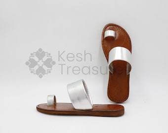 May include: A pair of silver leather sandals with a toe ring and two straps. The sandals have a brown leather sole.