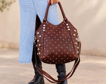 May include: A dark brown leather handbag featuring a slouchy silhouette, two top handles, and a detachable shoulder strap. The exterior is decorated with numerous silver-toned metal studs arranged in a grid pattern across the front surface.