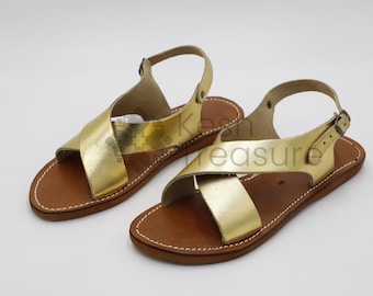 May include: A pair of gold leather sandals with criss-cross straps and brown leather soles.